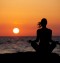 Silhouette of young woman in lotus position sitting on the beach and medditating